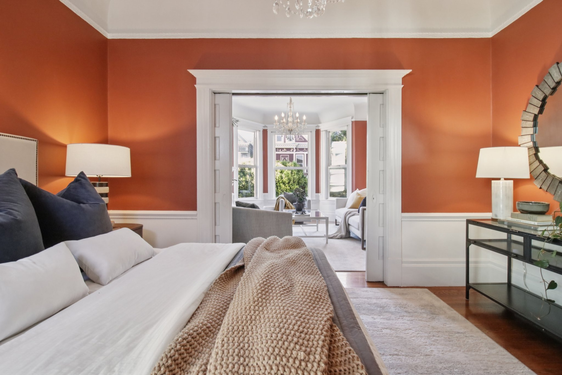 Warm orange bedroom with plush bedding and pocket-door view to a sunlit sitting room