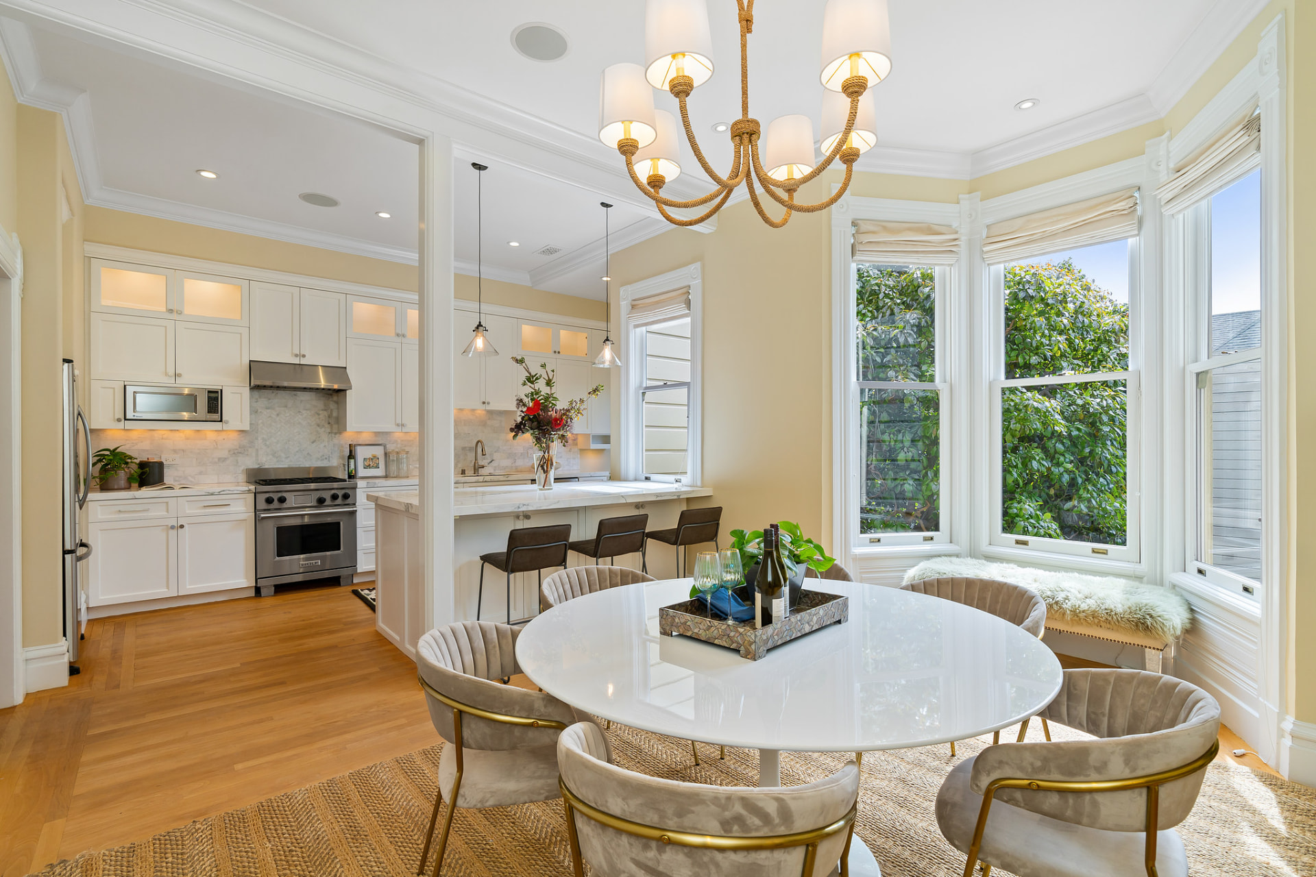 Bright kitchen and dining room with marble island, rope chandelier, and bay windows